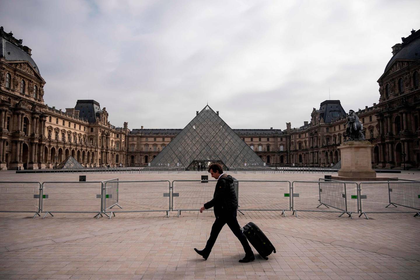 A man walks past the empty square at the Louvre Pyramid in Paris, on March on 17, 2020, while a strict lockdown comes into in effect in France to stop the spread of COVID-19, caused by the novel coronavirus. - A strict lockdown requiring most people in France to remain at home came into effect at midday on March 17, 2020, prohibiting all but essential outings in a bid to curb the coronavirus spread. The government has said tens of thousands of police will be patrolling streets and issuing fines of 38 to 135 euros (42-150 USD) for people without a written declaration justifying their reasons for being out. (Photo by Lionel BONAVENTURE / AFP)