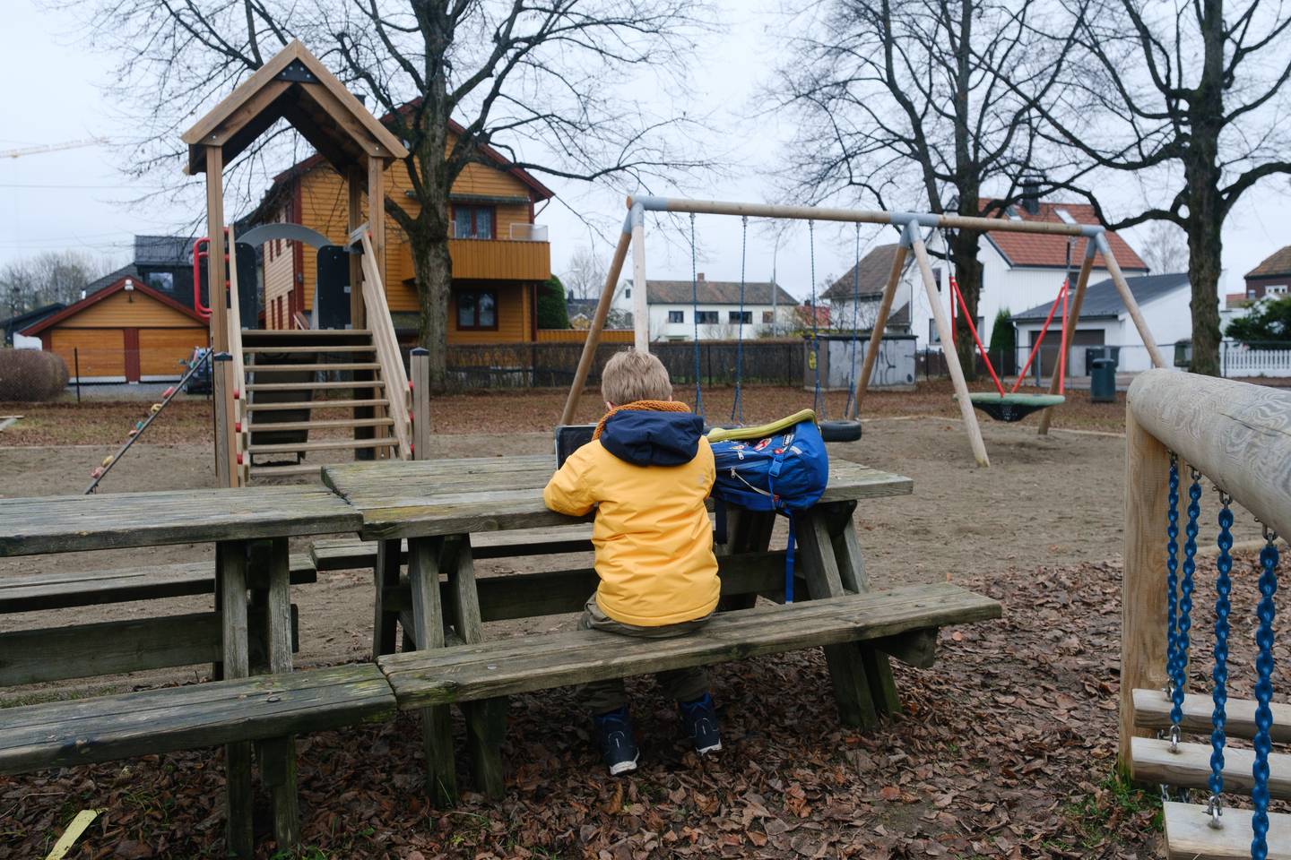 Barn med blå sekk alene på en lekeplass.