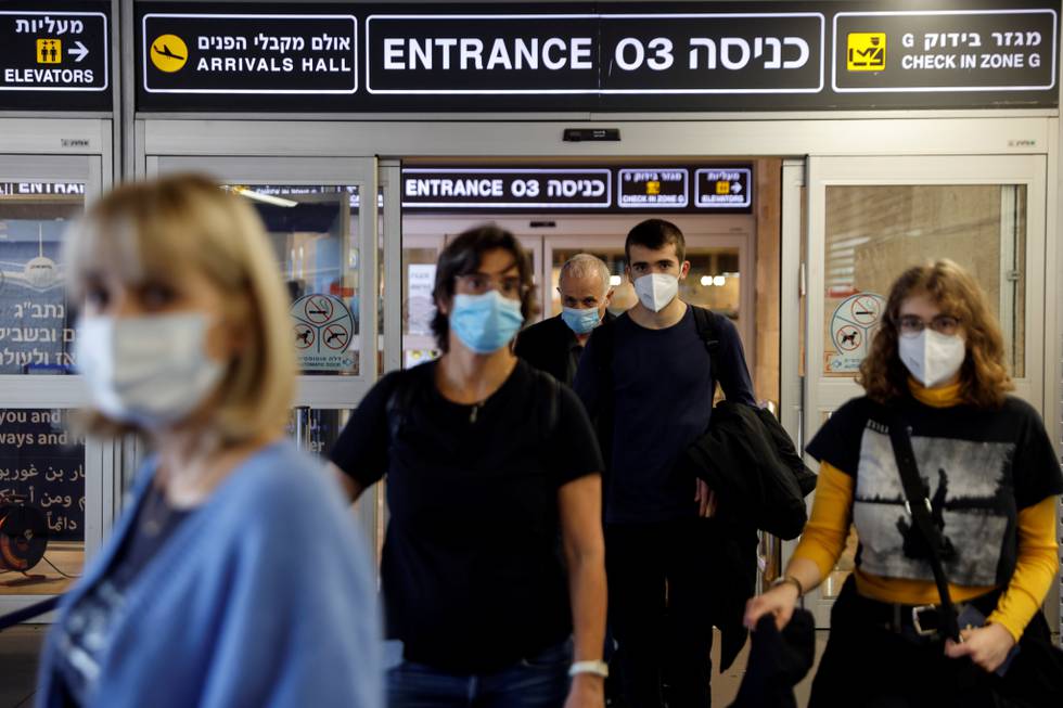 Fire personer med munnbind og trillekofferter på Ben Gurion-flyplassen utenfor Tel Aviv i Israel.