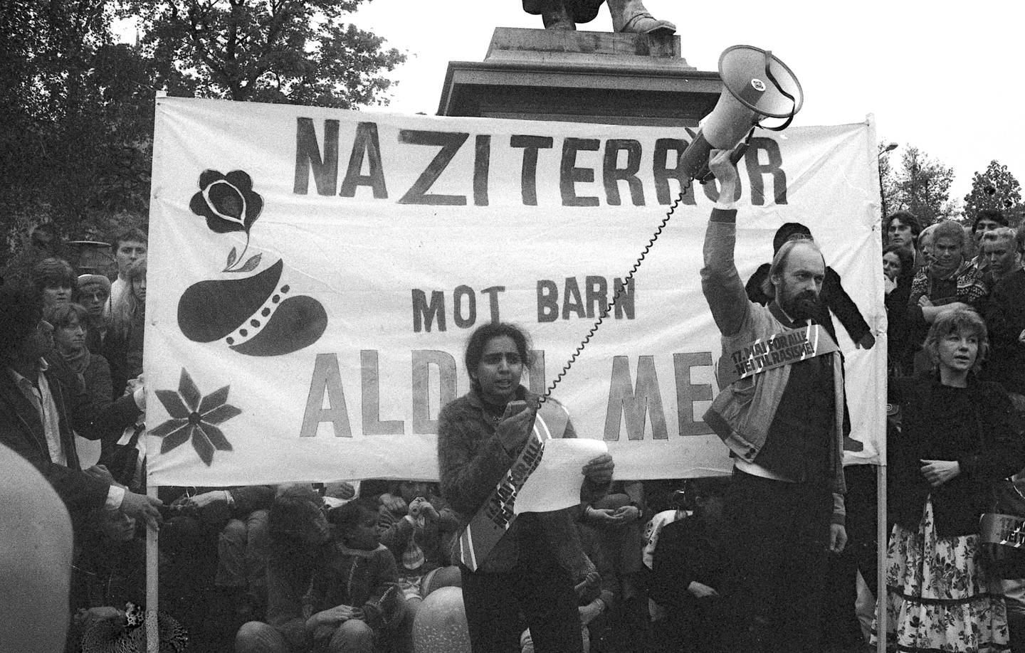 Salimi snakker inn i en ropert som en mann holder. Bak er et banner hvor det står Naziterror mot barn aldri mer.