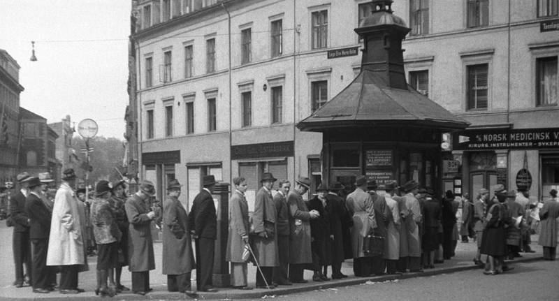 OSLO 19450509 Fredsdagene, Mai 1945. Folk i kø for å kjøpe aviser ved Narvesen-kiosken på Triangelen i Pilestredet. 