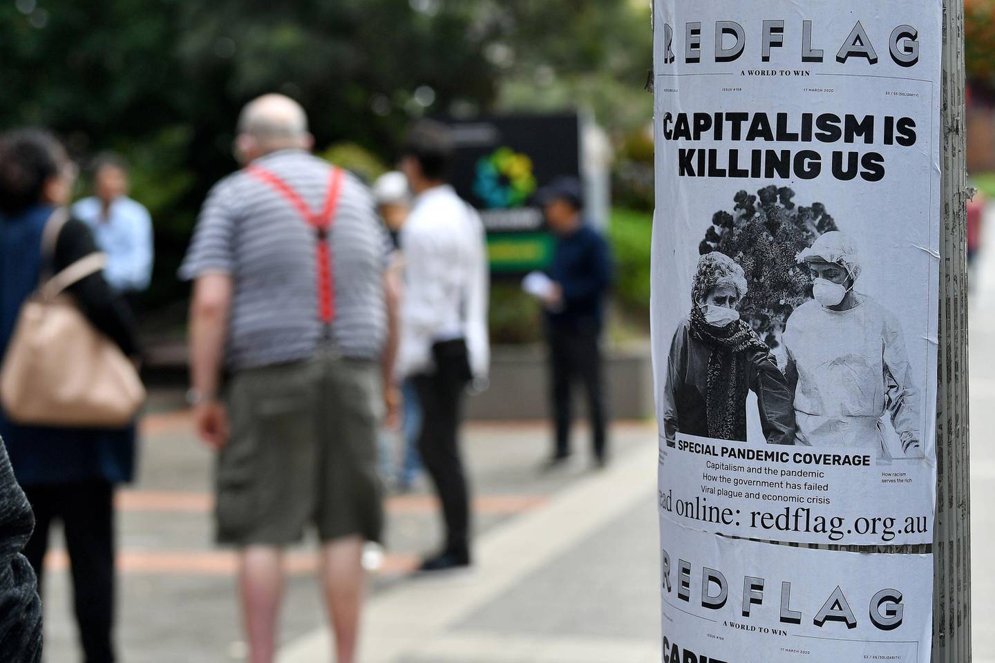 An anti-capitalist flyer is seen on a pole as people wait in a queue to receive benefit payouts, including unemployment and small business support as the novel coronavirus inflicts a toll on the economy, at a Centerlink payment centre in downtown Sydney on March 27, 2020. - The number of confirmed covid-19 cases in Australia passed the 3,000 mark on March 27, with the vast majority of infections in major east coast cities like Sydney, Brisbane and Melbourne. (Photo by Saeed KHAN / AFP)