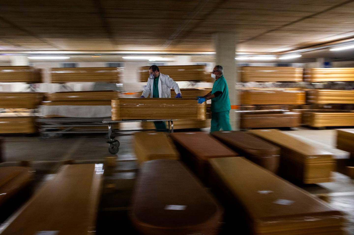 Workers move a coffin with the body of a victim of COVID-19 as other coffins are stored waiting for burial or cremation at the Collserola morgue in Barcelona, Spain, on April 2, 2020. (AP Photo/Emilio Morenatti)