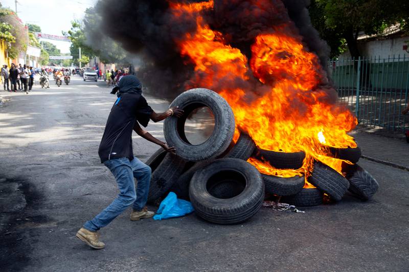 A protester tosses a tire onto a burning barricade during a protest demanding the release of political prisoners and the resignation of Haitian President Jovenel Moise in Port-au-Prince, Haiti, Wednesday, Dec. 16, 2020. (AP Photo/Dieu Nalio Chery)