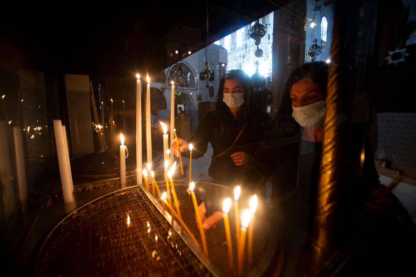 Christian worshippers light candles in the Church of the Nativity, traditionally believed to be the birthplace of Jesus Christ, in the West Bank city of Bethlehem, Monday, Nov. 23, 2020. Normally packed with tourists from around the world at this time of year, Bethlehem resembles a ghost town  with hotels, restaurants and souvenir shops shuttered by the pandemic. (AP Photo/Majdi Mohammed)