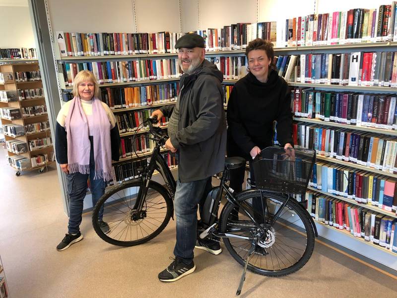 Lars Erik Henriksen hentet tirsdag ut den første elsykkelen til låns ved Onsøy bibliotek. Avdelingsleder Bente Bjerke (til venstre) og biblioteksjef Tora Klevås i Fredrikstad kommune er stolte av det nye tilbudet.