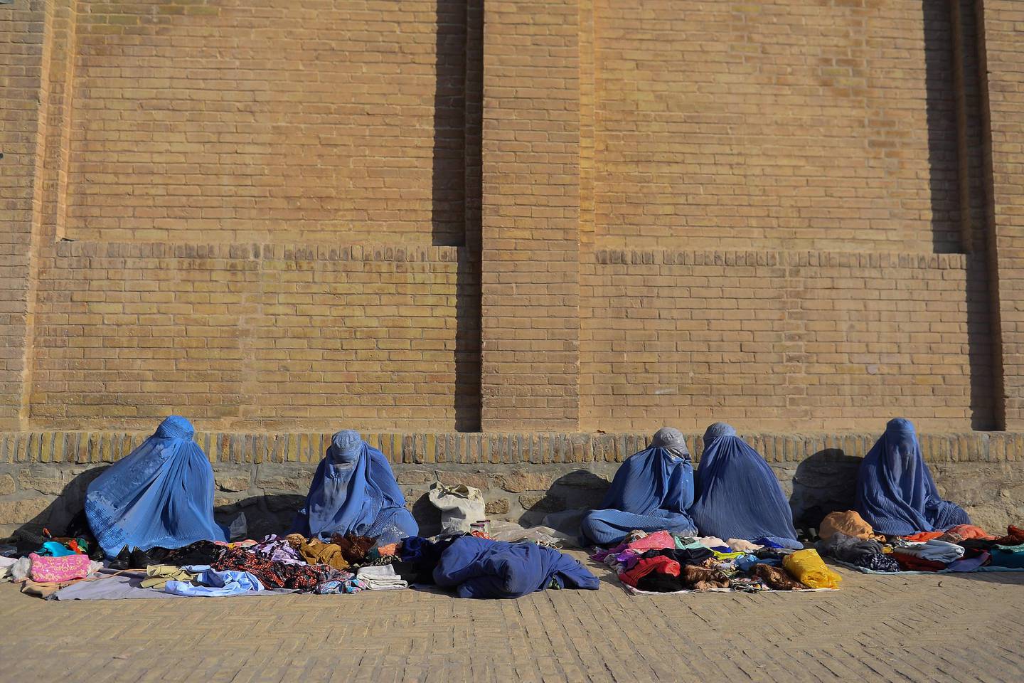 TOPSHOT - Women wearing burqas wait for customers as they sell clothes on a roadside in Herat on October 22, 2019. (Photo by HOSHANG HASHIMI / AFP)