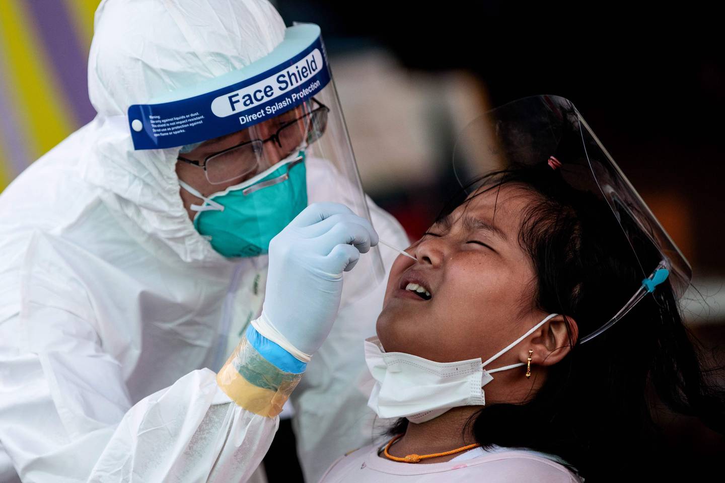 Medical officials conduct a nose swab test on a girl for the COVID-19 coronavirus at a seafood market in Samut Sakhon on December 19, 2020 after some new cases of local infections were detected and linked to a vendor at the market. (Photo by Jack TAYLOR / AFP)
