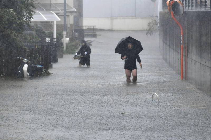People walk through a flooded street affected by Typhoon Hagibis, in Shizuoka, central Japan Saturday, Oct. 12, 2019. Tokyo and surrounding areas braced for a powerful typhoon forecast as the worst in six decades, with streets and trains stations unusually quiet Saturday as rain poured over the city. (Kyodo News via AP)