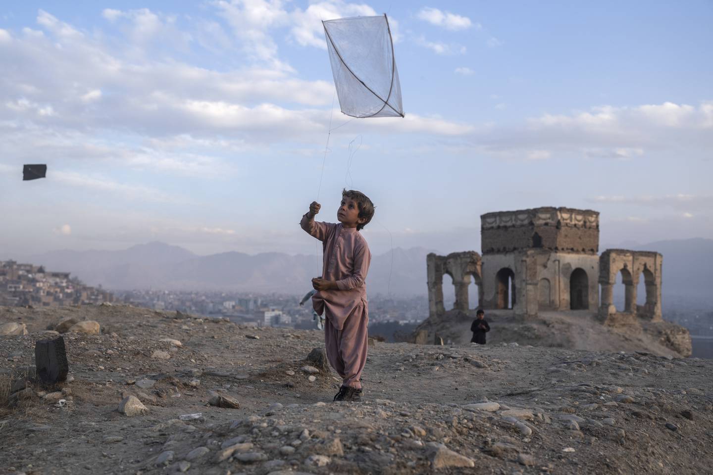 En gutt flyr en drage på en bakketopp i Kabul.