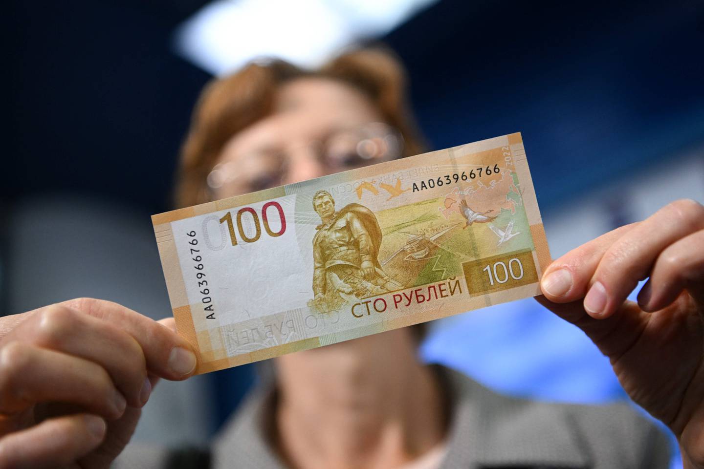 A woman shows an updated version of 100-rubles banknote during the official presentation in Moscow on June 30, 2022. (Photo by Natalia KOLESNIKOVA / AFP)