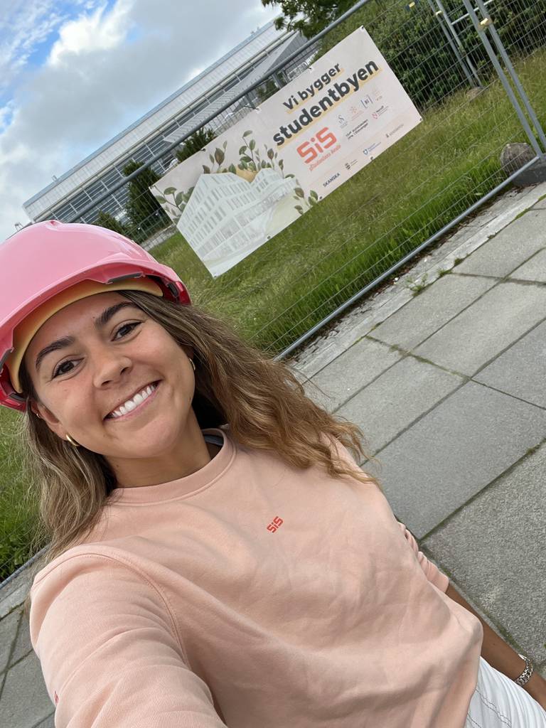 En jente i SiS genser med en rosa hjelm på hodet. Hun smiler.