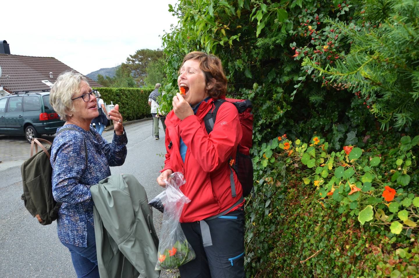 Hilde Grøtte (til høyre) er utdannet innen nyttevekst, og vet dermed hva som kan spises langs veien. Her tar hun et jafs blomster fra en hage sammen med Ingri Høiland.