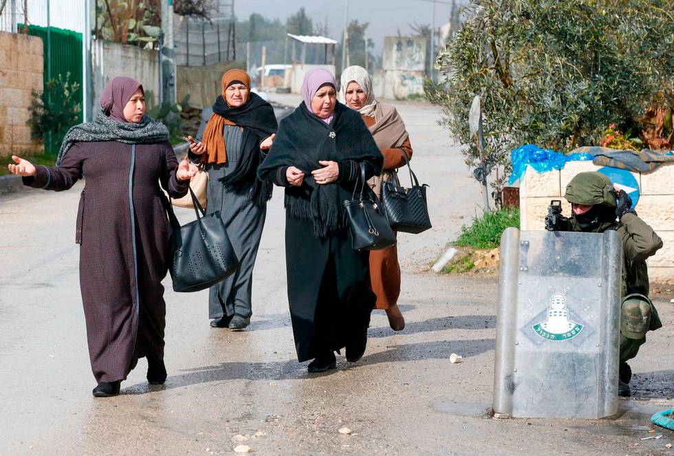 Palestinian women walk past an Israeli soldier during clashes with protesters following a demonstration in al-Aroub Palestinian refugee camp, between the West Bank towns of Hebron and Bethlehem, on January 29, 2020. - US President Donald Trump unveiled his controversial Israeli-Palestinian peace deal that staunchly favours Israel but offers Palestinians a pathway to a limited state. (Photo by HAZEM BADER / AFP)
