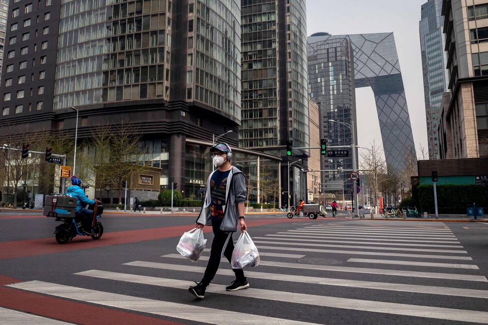 A man wearing a face mask amid the COVID-19 coronavirus outbreak crosses a street while carrying his groceries in Beijing on March 30, 2020. (Photo by NICOLAS ASFOURI / AFP)