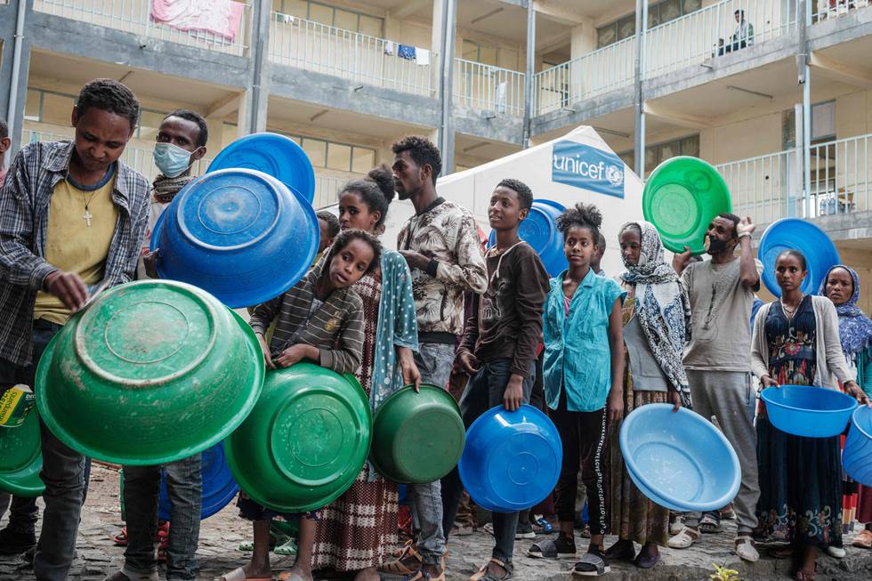 Mennesker med store blå og grønne plastbaljer venter i matkø i Etiopias Tigrayregion i juni i år.