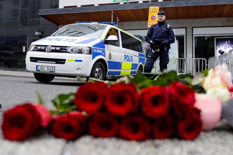 DAGEN ETTER: En politimann står like ved blomster og lys som er lagt ned ved varehuset Åhlens i Stockholm der en varebil braste inn og drepte fire mennesker fredag kveld.