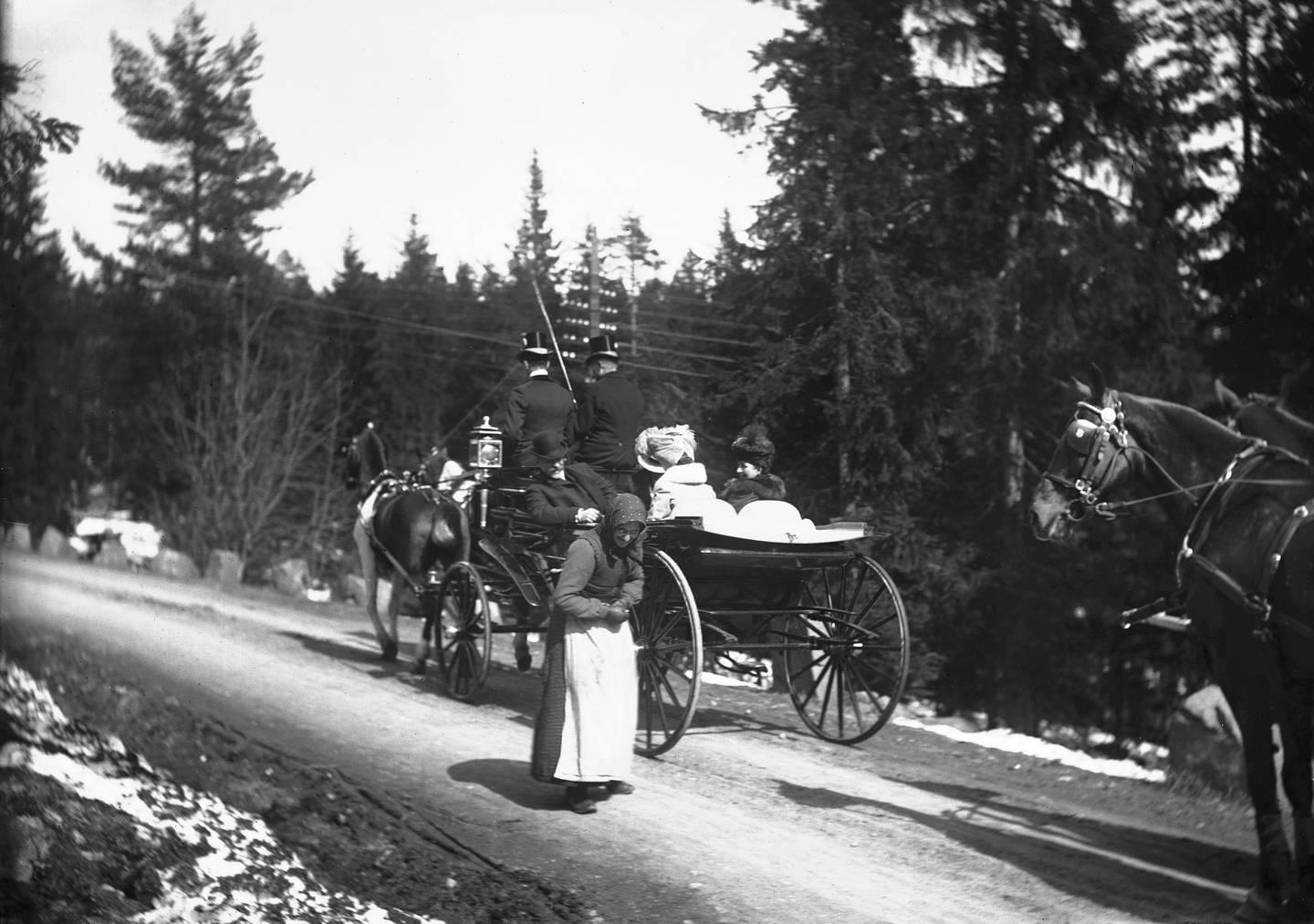Engelske kong Edward og dronning Alexandras var på Norgesbesøk i 1908. Her er de på Holmenkollen, som da lå i Aker kommune. Dronningen gir en almisse til en gammel tiggende kvinne.