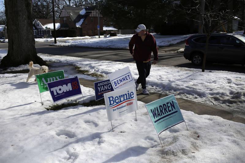 DES MOINES, IA - FEBRUARY 02: A man walking his dog walks past Democratic presidential campaign signs displayed in a front yard of a home campaign on February 2, 2020 in Des Moines, Iowa. Tomorrow, Iowa voters will go to their local precincts to caucus for a one of several presidential candidates.   Joshua Lott/Getty Images/AFP
== FOR NEWSPAPERS, INTERNET, TELCOS & TELEVISION USE ONLY ==