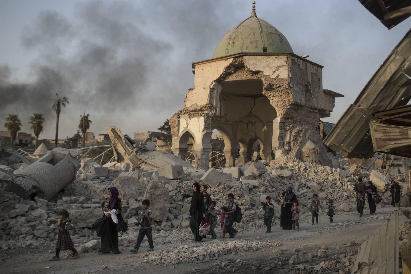 FILE - In this July 4, 2017, file photo, fleeing Iraqi civilians walk past the heavily damaged al-Nuri mosque as Iraqi forces continue their advance against Islamic State militants in Iraq's Old City of Mosul. The United Nations' cultural agency says reconstruction of Al-Nouri Mosque in Iraq's city of Mosul is scheduled to start at the beginning of 2020.  (AP Photo/Felipe Dana, File)