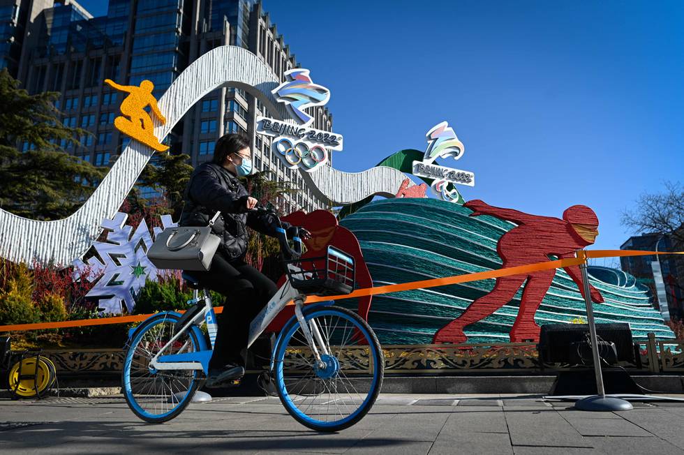 Syklist med munnbind sykler forbi en vinter-OL-installasjon der figurer går på skøyter ol.