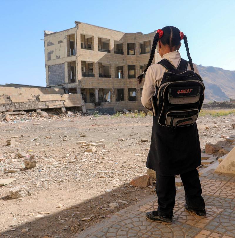 En skolejente står utenfor det som en gang var en skolebygning i byen Taez i Jemen. Jemen er et av landene som rammes verst av skoleangrep, og krigen har mer enn doblet antall barn som ikke får gå på skole.