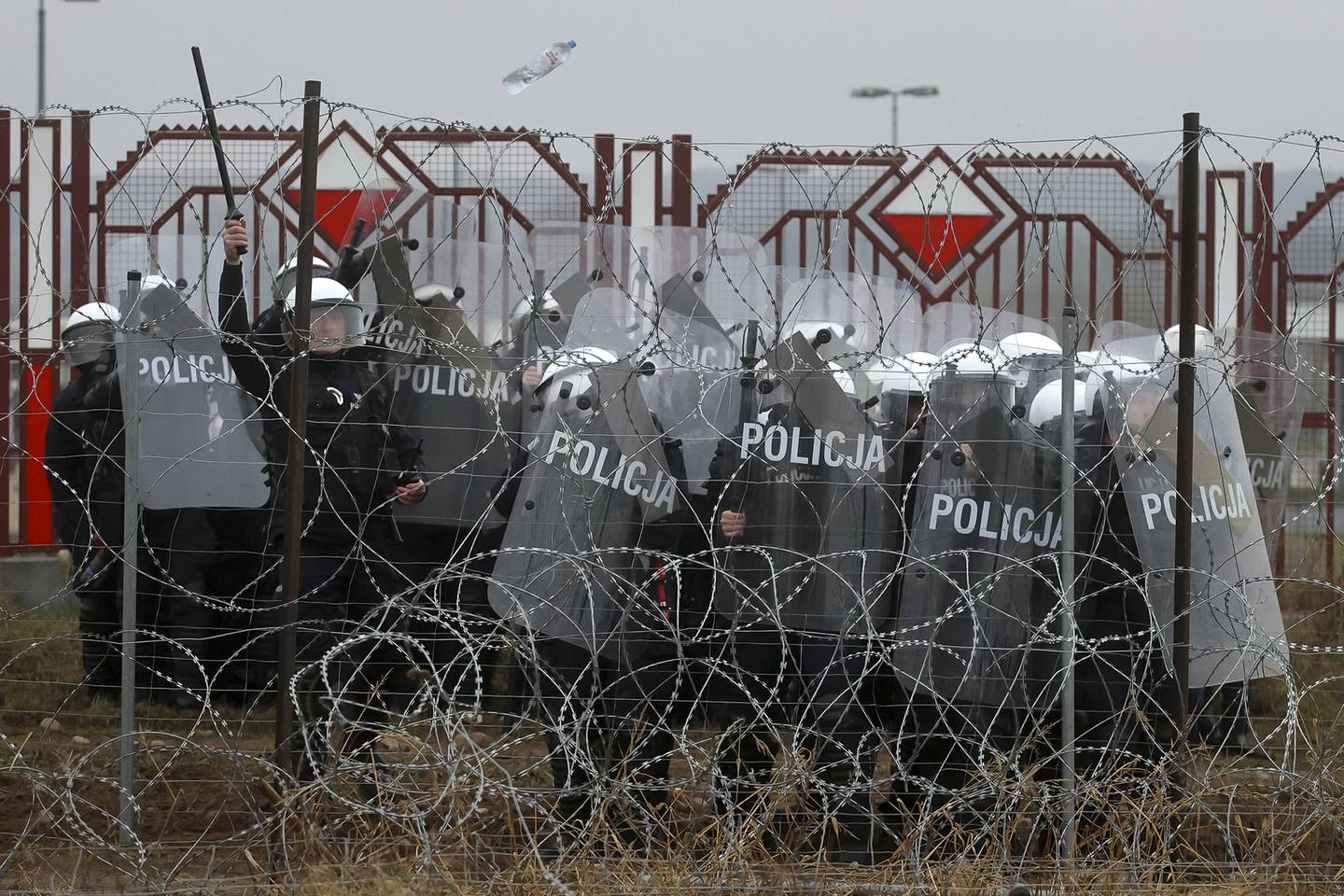 Polske tjenestemenn bak et piggtrådgjerde etter sammenstøt med migranter ved grensa.