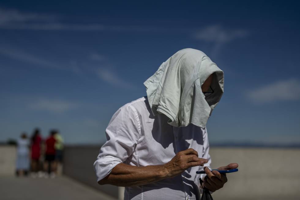 Bildet er av en mann som dekker hodet med en jakke for å beskytte det mot varmen fra solen i Madrid. Han står med en mobiltelefon. Spania er inne i årets første hetebølge. Foto: Manu Fernandez / AP / NTB