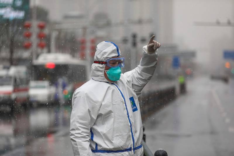 A worker wearing a protective suit gestures to a driver outside a tumor hospital newly designated to treat COVID-19 patients in Wuhan in central China's Hubei Province, Saturday, Feb. 15, 2020. The virus is thought to have infected more than 67,000 people globally and has killed at least 1,526 people, the vast majority in China, as the Chinese government announced new anti-disease measures while businesses reopen following sweeping controls that have idled much of the economy. (Chinatopix via AP)