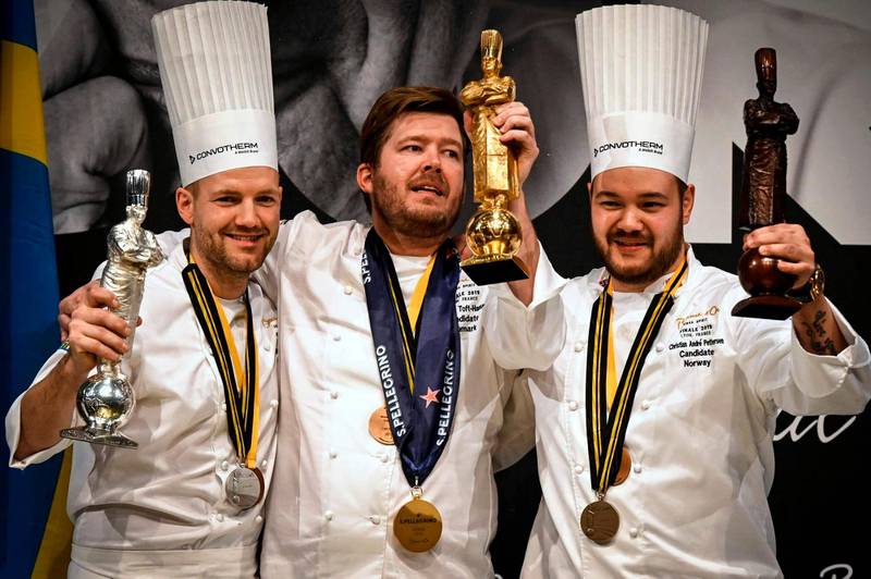 First place winner Danish chef Kenneth Toft-Hansen (C), second-placed Swedish chef Sebastian Gibrand (L) and third-placed Norwegian chef Christian Andre Pettersen (R) hold their trophies as they celebrate on the podium after competing in the final event of the Bocuse d'Or International culinary competition during SIRHA, an international hospitality and food trade show, on January 30, 2019, in Chassieu, outside Lyon. (Photo by JEAN-PHILIPPE KSIAZEK / AFP)