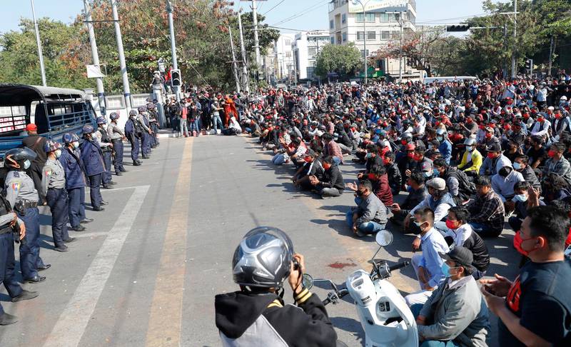 Protesters sitting on a road blocked by police in riot gear flash the three-fingered salute, a symbol of resistance, during a protest in Mandalay, Myanmar, Tuesday, Feb. 9, 2021. Protesters continued to gather Tuesday morning in major cities breaching Myanmar's new military rulers ban of public gathering of five or more issued on Monday intended to crack down on peaceful public protests opposing their takeover. (AP Photo)