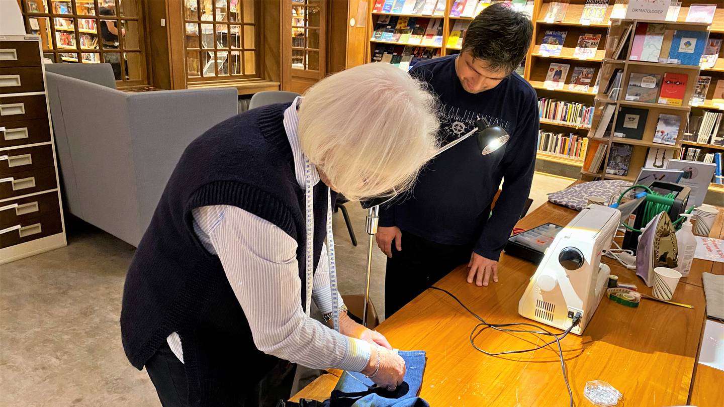 Berit Stene fra Norske Kvinners Sanitetsforening hjelper Unvery med å legge opp en bukse på «Søm & kaffe» ved Fredrikstad bibliotek.