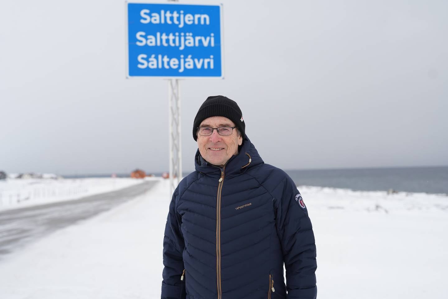 Einar Niemi foran skiltet der han bor i Varanger. Skiltet er på norsk, samisk og kvensk.