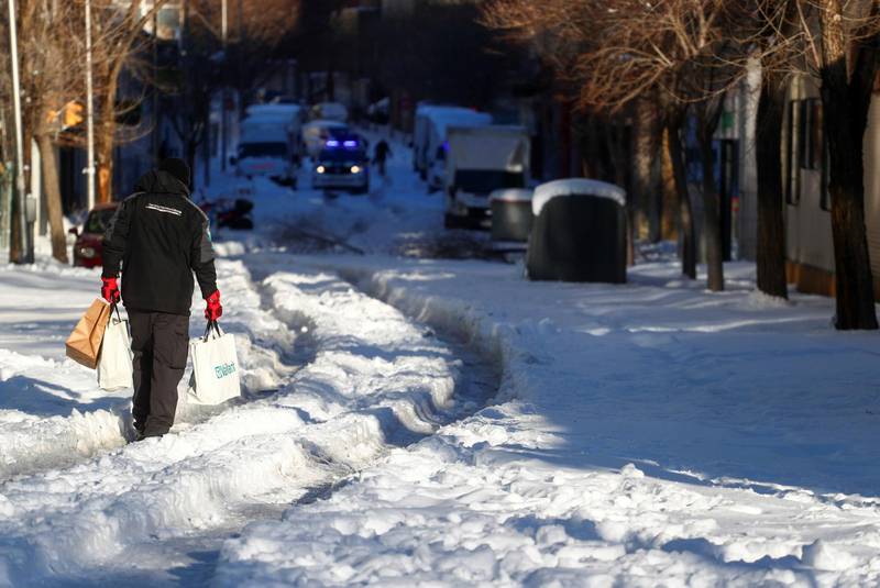 A person holding bags walks through a snow-covered street after heavy snowfall in Madrid, Spain, January 11, 2021. REUTERS/Sergio Perez