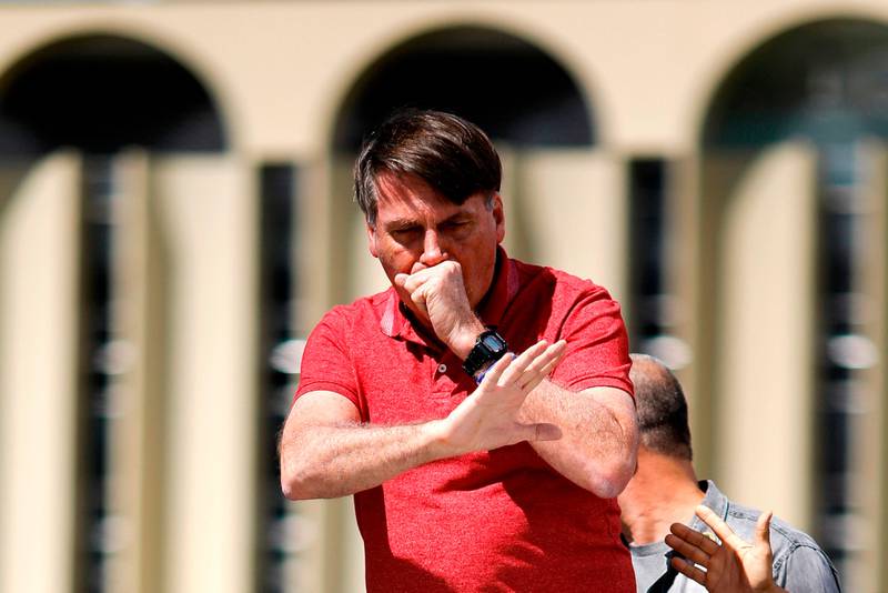 TOPSHOT - Brazilian President Jair Bolsonaro coughs as he speaks after joining his supporters who were taking part in a motorcade to protest against quarantine and social distancing measures to combat the new coronavirus outbreak in Brasilia on April 19, 2020. (Photo by Sergio LIMA / AFP)