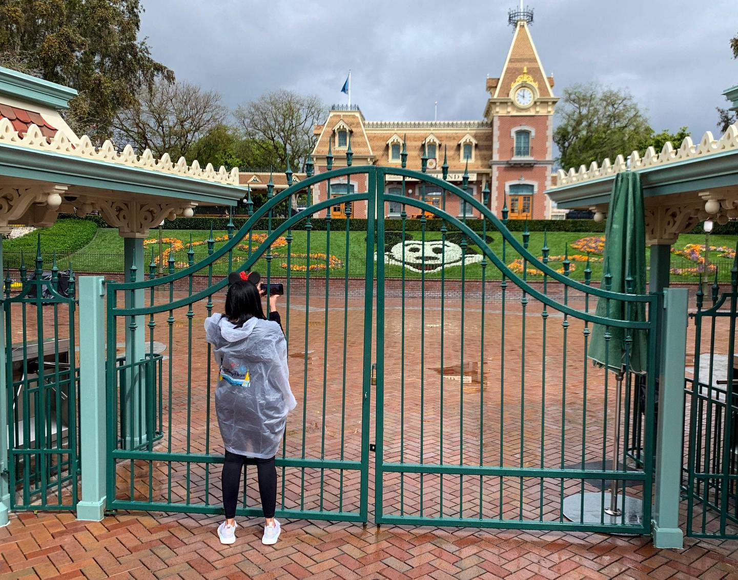 A visitor to the Disneyland Resort takes a picture through a locked gate at the entrance to Disneyland in Anaheim, Calif., on Monday, March 16, 2020.  Disneyland Resort is shutting down due to the new coronavirus outbreak. For most people, the new coronavirus causes only mild or moderate symptoms, such as fever and cough. For some, especially older adults and people with existing health problems, it can cause more severe illness, including pneumonia. The vast majority of people recover. (Jeff Gritchen/The Orange County Register via AP)