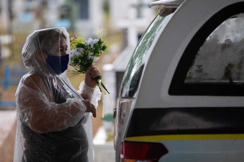 A relative of a COVID-19 victim holds flowers next to a hearse at the Nossa Senhora Aparecida cemetery in Manaus, Amazonas state, Brazil, on January 13, 2021, amid the novel coronavirus pandemic. - In Manaus there is a shortage of hospital beds as cases increased at an alarming rate. The city, with two million inhabitants, had already experienced nightmarish scenes in April and May, with mass graves and refrigerated trucks parked in front of hospitals to pile up the dead. But the situation is even worse in the beginning of 2021, since between January 1 and 11, at least 1,979 people were admitted to hospitals due to the virus, against 2,128 for the whole month of April, the worst since the start of the pandemic. (Photo by MICHAEL DANTAS / AFP)