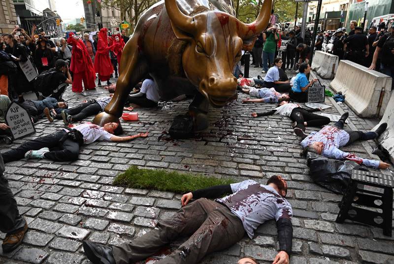 Protestors covered in fake blood gather around the Wall Street Bull during an  ?Extinction Rebellion? demonstration in New York on October 7,2019. - The rally is part of a global network of protests and events around the globe this week to raise awareness of the climate crisis' potentially disastrous effects. (Photo by TIMOTHY A. CLARY / AFP)