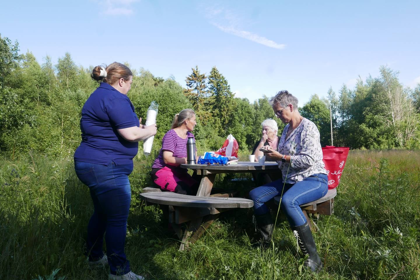 Fire kvinner sitter ved et piknikbord og drikker kaffe
