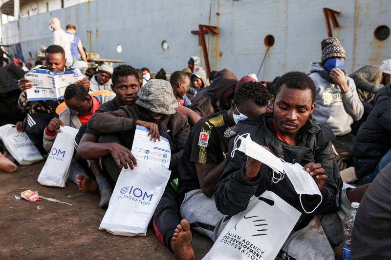 Migrants rescued off the coast of al-Khums, about 120 kilometres east of the capital, receive aid packages (including surgical masks for the COVID-19 coronavirus pandemic) as they sit on the pier in Tripoli's naval base on February 10, 2021. (Photo by - / AFP)