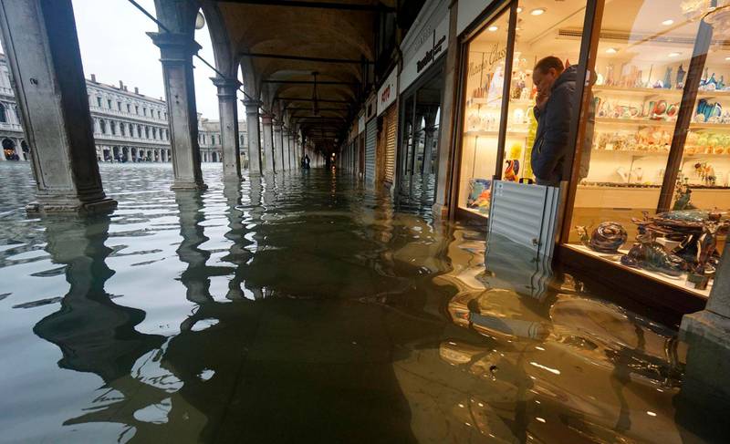 A shopkeeper looks out of his shop at a flooded St. Mark's Square on the occasion of a high tide, in Venice, Italy, Tuesday, Nov. 12, 2019. The high tide reached a peak of 127cm (4.1ft) at 10:35am while an even higher level of 140cm(4.6ft) was predicted for later Tuesday evening. (Andrea Merola/ANSA via AP)