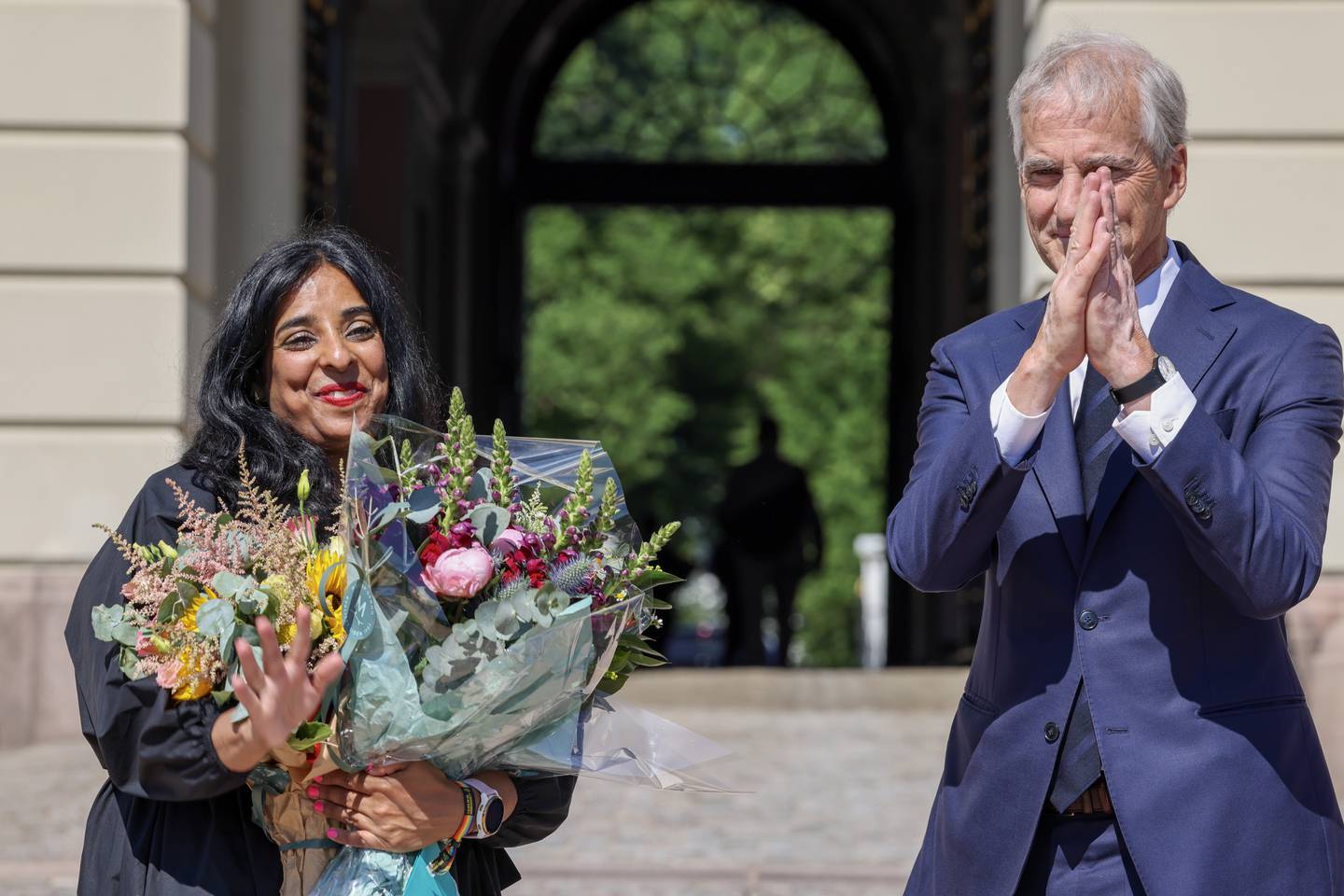 Lubna Jaffery sammen med statsminister Jonas Gahr Støre etter han presenterte henne som ny kultur- og likestillingsminister onsdag 28. juni. Hun står med blomster og smiler, mens Støre har hendene foran ansiktet og klapper.
