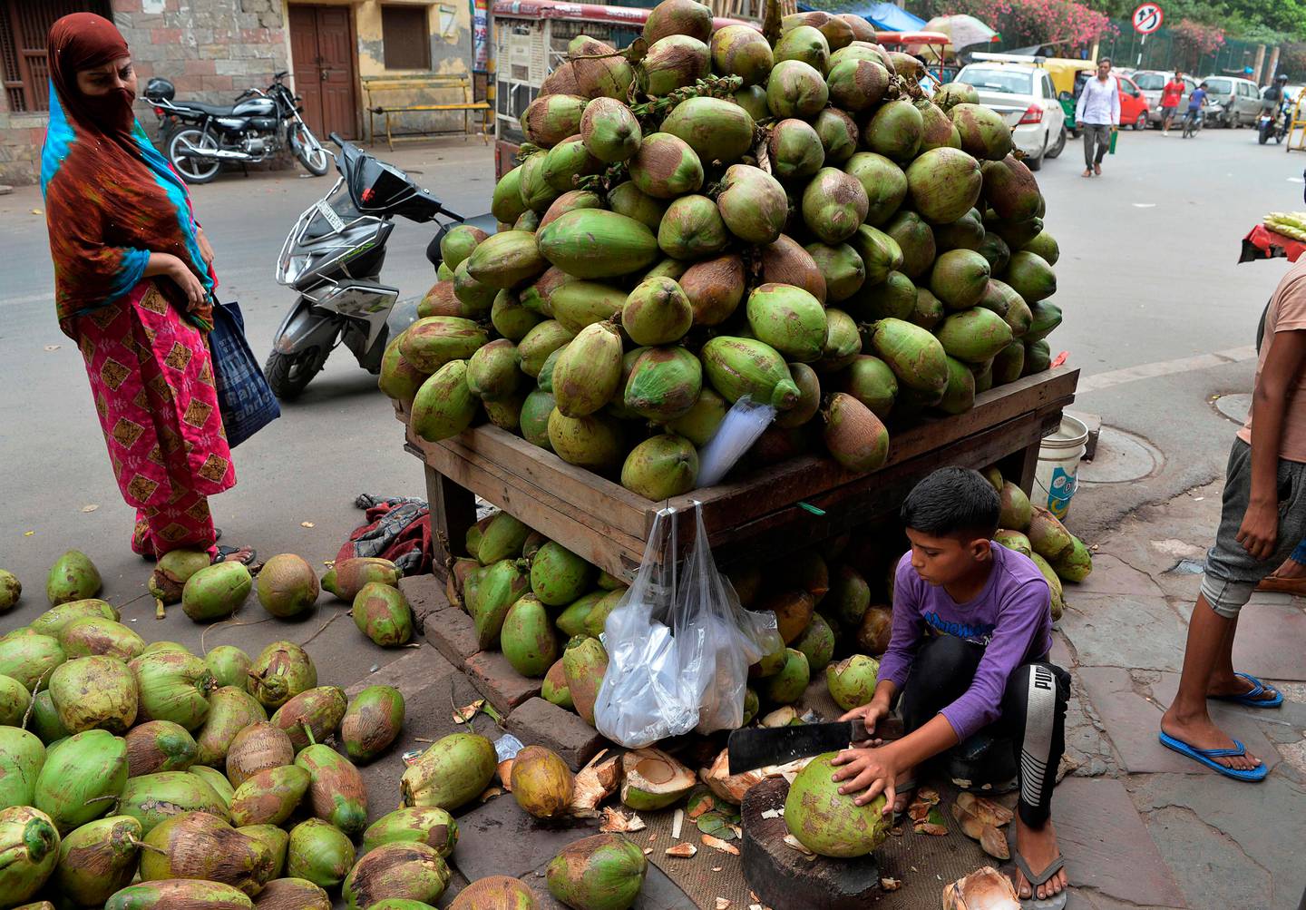 An Indian vendor cuts coconuts for a customer at a roadside in the old quarters of New Delhi on July 14, 2019. - Coconut water is in high demand during the summer months in India. (Photo by Sajjad HUSSAIN / AFP)