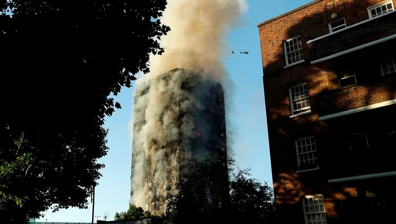 Røyk stiger opp fra den 24 etasjer høye boligblokken som brenner i London. Et helikopter svever over blokken for om mulig å redde ut beboere.