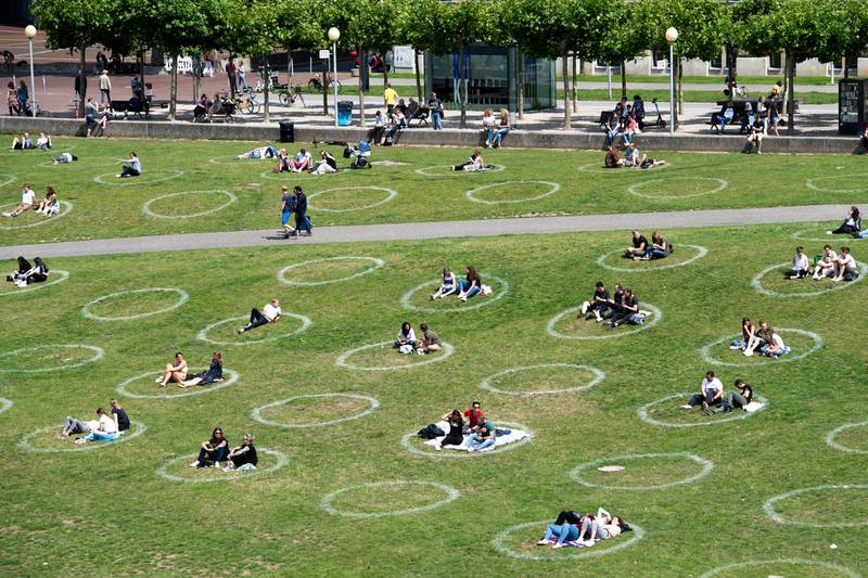 People sit in painted circles on a meadow on the banks of the Rhine in Cologne, Germany, on Saturday, July 11, 2020. The circles are to ensure that the minimum distance is maintained during the corona pandemic. (Marius Becker/dpa via AP)