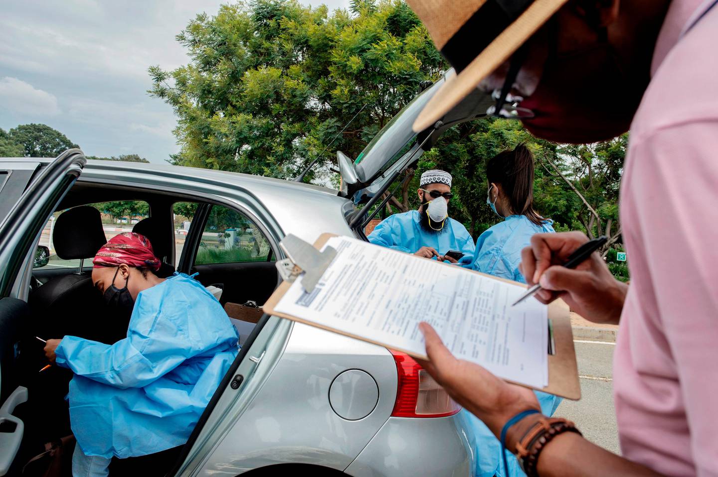 A patient (R) fills out a form before being tested by Lab Technician from the Mullah Laboratories during a drive through COVID-19 swab test campaign at the testing spot at the Flower Hall parking, at Wits University, Braamfontein, Johannesburg, on January 5, 2021. (Photo by Luca Sola / AFP)