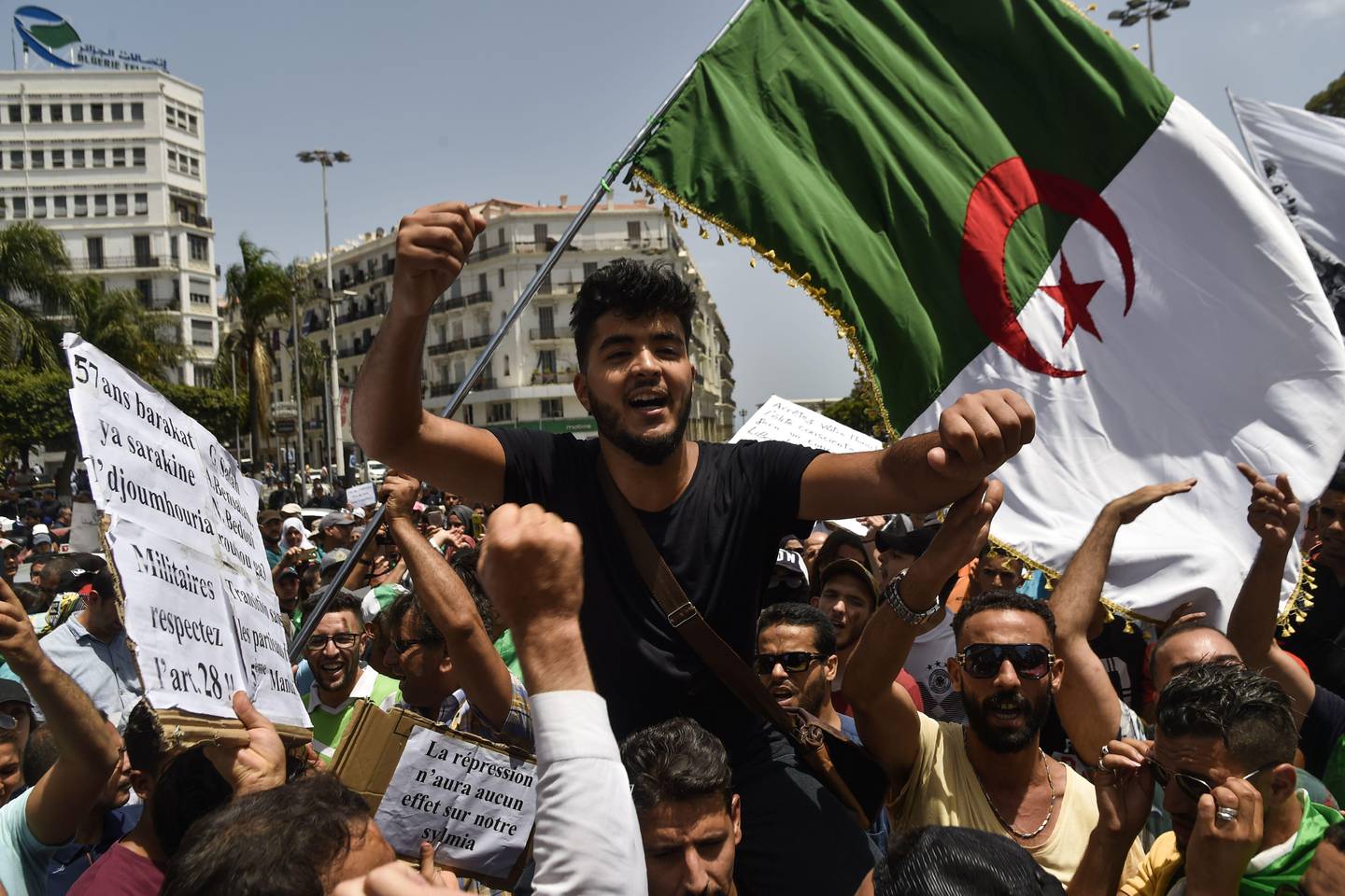Algerian demonstrators wave a national flag and carry placards staing their demands as they take part in a protest in the streets of the capital Algiers on July 9, 2019. - Hundreds of Algerian students and teachers demonstrated today for the 20th consecutive week, demanding a "regime change" and the release of "political detainees," said an AFP journalist. (Photo by RYAD KRAMDI / AFP)