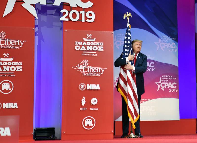 TOPSHOT - US President Donald Trump hugs the US flag as he arrives to speak at the annual Conservative Political Action Conference (CPAC) in National Harbor, Maryland, on March 2, 2019. (Photo by Nicholas Kamm / AFP)