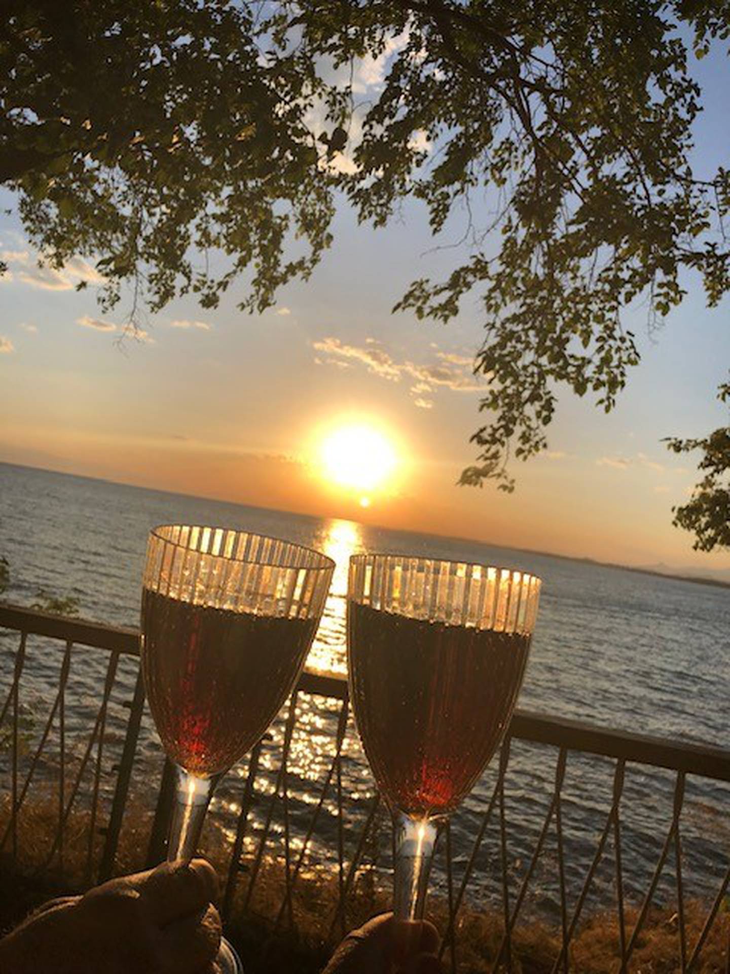 To vinglass mot hverandre med hav og solnedgang i bakgrunnen.