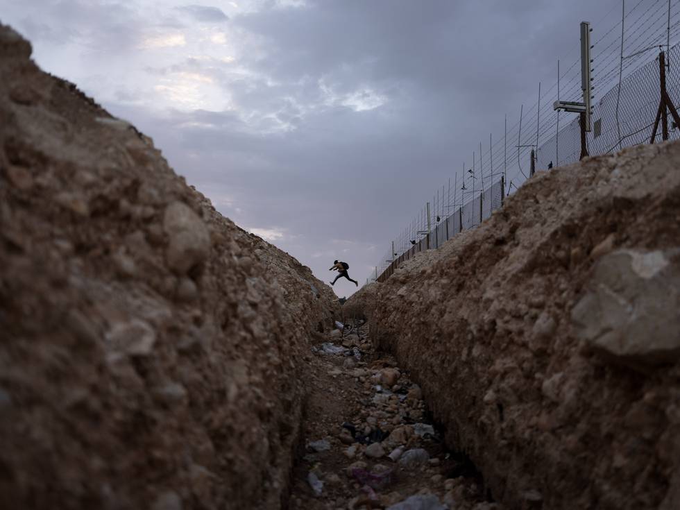 En palestinsk mann tar seg inn i Israel gjennom et hull i delingsmuren, som her er et gjerde, på Vestbredden. 20 år har gått siden Israelerne satte opp det som skulle være en midlertidig løsning. Foto: Oded Balilty / AP / NTB